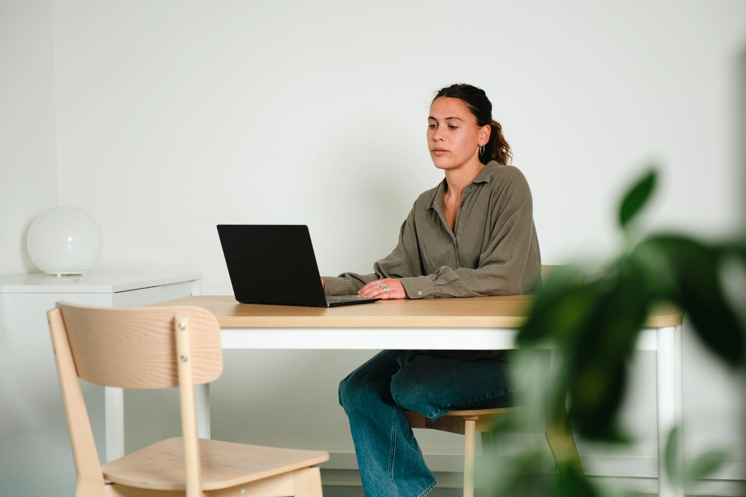 KONTEXT JUGEND – Rechtspsychologin – Eine Frau in einem grauen Shirt sitzt an einem Schreibtisch und arbeitet an einem Laptop in einem hellen, schlicht eingerichteten Raum.